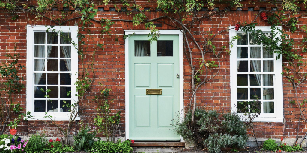 Charming red-brick house with green door, white-framed windows, and vibrant climbing plants and flowers